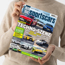 Eine Person im beigefarbenen Strickpullover hält eine schräg ausgerichtete Zeitschrift mit dem Titel „Auto Bild sportscars“. Das Cover zeigt mehrere rote, blaue, gelbe, weiße und grüne Sportwagen sowie die Aufschriften „VERGLEICHSTEST“, „TECHNOLOGIE“, „Audi RS 5 HYBRID und Elektro Hyundai Ioniq 6 N gegen Verbrenner BMW M3 Competition“, „GEWINNSPIEL“ und „HAUSBESUCH“.