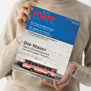 Person in beigem Strickpullover hält die Zeitschrift „mare – Die Zeitschrift der Meere“, Ausgabe Nr. 169. Titelbild zeigt eine weiße Betonmauer mit rotem Linienbus im unteren Bereich, darüber blaue Fläche mit Texten: „Drei Tage im Südpolarmeer“, „Die Lagune von Venedig“, „Die Klippenspringer von Acapulco“ und Haupttitel „Die Mauer – Japans Jahrhundertbauwerk zum Schutz gegen Tsunamis“.