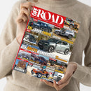 Person in beigem Strickpullover hält eine Ausgabe des Magazins „OFF ROAD – Das 4x4-Magazin für die Freiheit auf Rädern“ mit rotem Titelkopf. Auf dem Cover sind mehrere Geländewagen, darunter ein schwarzer XXL-Luxus-Truck, ein grauer SUV und ein orangefarbener Offroader sowie Schriftzüge wie „Die dritte Generation“, „Förster, die sechste“ und „Algerien“ zu sehen, umgeben von kleineren Bildern zu Testberichten und Reisethemen.