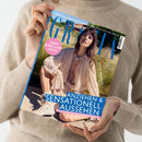 Person in beigem Strickpullover hält eine Ausgabe des Magazins „Grazia“ mit Titelbild einer sitzenden Frau in hellbeiger, tief ausgeschnittener Bluse und auffälliger Halskette, im Hintergrund grüne Wiese und blauer Himmel. Sichtbare Texte: „HIGH JEWELLERY ISSUE“, „ANZIEHEN & SENSATIONELL AUSSEHEN“, „DIE 50 SCHÖNSTEN SOMMERKLEIDER“, „MOST WANTED“, sowie eine weiße Kopfzeile mit Modetipps zur Fußball-WM.