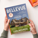 Titelbild des Magazins „BELLEVUE“ mit blauem Hintergrund und einem Foto eines reetgedeckten Backsteinhauses mit Garten und Terrasse in der Mitte. Textaufschriften: „Europas größtes Immobilien-Magazin“, „Großes Special Hamburg“, „Weltweit Häuser unter 250.000 Euro“, „Lieblingsinsel – Sylt zwischen Sehnsucht und Realität“, sowie Themen zu Österreich, Spanien und New York. Zwei Hände halten das Magazin auf einem weißen Tisch neben einem orangefarbenen Tablett.