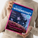 Weibliche Person in beigefarbenem Strickpullover hält eine schräg abgebildete Zeitschrift mit pinkem Rand. Das blaue Cover trägt den Titel „BILD DER WISSENSCHAFT“ und zeigt eine mikroskopische Aufnahme von Immunzellen; sichtbar sind außerdem „Unser Immunsystem“, „Bestäuber“, „Limes“, „Smart Home“ und ein Textfeld „Im Fokus: Monde“.