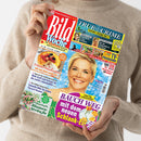 Zwei Hände halten eine schräg liegende, glänzende Zeitschrift vor einem beigefarbenen Strickpullover. Auf dem Cover stehen „Bild der Frau Woche“, „TRUFFLE CRIME“, „TATORT PROMI-WELT“, „Winona Ryder“, „Robert Downey Jr.“ und „BAUCH WEG mit dem neuen Schlank-Eis“; abgebildet sind ein weibliches Gesicht, Käsekuchen, Blumen und Eis.
