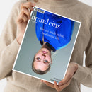 Weibliche Person mit beige gestricktem Pullover hält ein schräg und auf dem Kopf stehendes Magazin vor grauem Hintergrund. Das blaue Cover trägt den Titel „brand eins“, den Untertitel „Das geht!“ und die Aufschrift „Wie du mich siehst, bestimme ich.“; oben steht „brand eins“, „28. Jahrgang“ und „August 2026“.