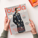 Aufsicht auf eine leicht schräg liegende burda style-Nähzeitschrift, die von zwei Händen gehalten wird; auf dem Cover eine weibliche Person in einem dunkelblauen Mantel mit großen hellen Punkten und Brosche. Sichtbare Texte: „NÄHEN AUS LEIDENSCHAFT“, „Wow! Großes Runway Special“, „DEEP PURPLE“, „ICONIC FASHION MOMENT“, „POWER LOOKS“ und „HERBST TRENDS!“. Oben rechts liegt ein orangefarbenes Kunststofftablett mit orangefarbenem Werkzeug.