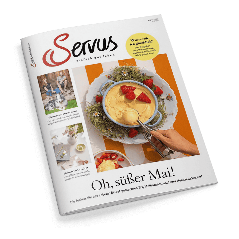Titelbild der Zeitschrift „Servus – einfach gut leben“ mit einer Nahaufnahme von Vanilleeis in einer blauen Schüssel, garniert mit frischen Erdbeeren, auf einem mit Gräsern dekorierten Tablett; daneben eine rechte Hand mit Eiskugelportionierer; Schlagzeile: „Oh, süßer Mai!“, weitere Texte: „Wie werde ich glücklich?“, „Wohnen im Dreiseithof“, „Heimat im Quadrat“.