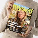 Person in beiger Strickjacke hält das Magazin „myself“ (Ausgabe März 2023) mit einer weiblichen Person auf dem Cover, die eine braune Jacke mit Reißverschluss trägt. Aufschriften: „Ich fühle mich wohl mit mir“, „Willst du irgendwann Kinder?“, „Neues von der Schilddrüse“, „Fröhlich, stylish, bunt“, „Mehr Begeisterung, bitte!“, „Beach-Body ohne Stress“ und „20 Jahre myself“. Hintergrund in warmen Beige‑ und Grüntönen.