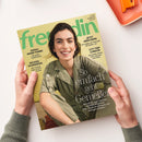 Titelblatt der Zeitschrift „freundin“ mit hellgrünem Hintergrund; im Mittelpunkt eine lächelnde weibliche Person mit dunklen Haaren in olivgrüner Jacke. Textaufschriften u. a.: „So einfach geht Genießen“, „GENAU MEINE FARBE!“, „RÜCKEN-SCHMERZEN“, „JETZT ABSICHERN“, „CITY-TRIP LONDON“. Gehalten von zwei Händen über weißer Oberfläche mit orangefarbenem rechteckigem Objekt am oberen Bildrand.