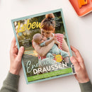 Titelbild des Elternmagazins „Leben & erziehen“ mit einer weiblich gelesenen Person in rot-weiß gestreiftem Oberteil, die ein lachendes Baby in einem mintfarbenen Strampler im Arm hält; Hintergrund unscharf mit grünlich-gelben Naturtönen. Abgedruckte Texte: „Endlich draußen“, „Im Schlummer-Modus – Dieser Trick hilft beim Einschlafen“, „Ordnung schaffen – So bekommt ihr das Chaos in den Griff“ und „Sprich Klartext!“.