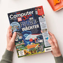 Schräg gehaltene Zeitschrift „Computer Bild“ mit blauem Digitalmuster, roter „Bild“-Kennzeichnung und der Aufschrift „30 Jahre – Der FRITZ!BOX-WÄCHTER“; sichtbar sind Themen zu Google Pixel, Fotosammlung, Outdoor-Technik, Top-Apps für den Schulstart und Samsung-Fitnesstrackern. Zwei Hände halten das Magazin vor hellem Hintergrund, oben rechts liegt ein orangefarbenes Gerät.