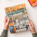 Auf weißem Tisch von zwei Händen gehaltenes Einrichtungsmagazin „COUCH“ mit orangefarbener Titelschrift und Coverfoto einer Frau mit weißem Hund in einem Wohnzimmer. Sichtbare Texte: „ALLES, WAS DU LIEBST“, „FERIENFLAIR ZU HAUSE“, „URLAUBS-VIBES“, „EURO-SUMMER“, „MEERESFARBEN“, „Coolcation“, „Strandgut upgraden“ und „Perfekte Reisebegleiter“; oben rechts liegt ein orangefarbenes Tablett.