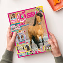 Titelblatt des Magazins „Lissy“ mit großem Foto eines braunen Pferdes im Galopp auf steinigem Untergrund. Drumherum bunte grafische Elemente und Textfelder mit Aufschriften wie „Teste dein Lissy-Wissen!“, „Coole Punkte – Appaloosa“, „Fotoroman – Lola in Gefahr“, „2 bezaubernde Poster!“ sowie ein Hinweis auf eine neue Serie. Das Heft liegt in zwei Händen auf hellbeiger Tischoberfläche.