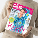 Zwei Hände in beigefarbenem Strickpulli halten das Magazin „plus magazin“ mit pinkem Titelkopf; auf dem Cover eine lächelnde Frau in blauer gemusterter Bluse vor hellblauem Hintergrund. Sichtbare Texte: „Gutes für den Darm“, „Bezaubernder Bodensee“, „50+ Die besten Krankenkassen“, „Die Natur schenkt uns neue Kraft“, „Sommer-Mode“ und „Kinder, wie die Zeit vergeht“.