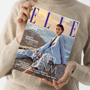 Person in beigem Strickpullover hält eine Zeitschrift mit dem Titel „ELLE“ (Ausgabe Juni 2025). Auf dem Cover sitzt eine weibliche Person mit hellblauem Blazer und heller Jeans auf Felsen vor einem Meer bei Sonnenuntergang. Sichtbare Texte: „GENERATION LOVE – Was Mütter und Töchter voneinander lernen können“, „BEAUTY MASTERCLASS – Sunny Glow, Skin Drops, perfekte Lippen“, „SOMMER DENIM – neue Silhouetten, perfekte Schnitte, unschlagbare Kombis“.