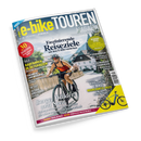 Titelbild des Magazins „e-bike TOUREN“ Ausgabe 02-25, Frühling/Sommer. Im Vordergrund fährt eine Person mit rotem Trikot, schwarzer Shorts und Helm auf einem schwarzen E-Bike eine Dorfstraße entlang, im Hintergrund Häuser, Bäume und Berge. Sichtbare Textelemente: „Faszinierende Reiseziele mit dem E-Bike entdecken“, „Berge, Wälder und Seen“, „Radfahren in Österreich“, „E-Bike Highlights 2025“.