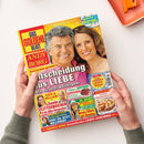 Deutschsprachige Zeitschrift „Das goldene Blatt“ mit Titelbild eines lächelnden Mannes und einer lächelnden Frau, rotem und gelbem Cover sowie großen Schlagzeilen wie „Entscheidung aus Liebe“, „Andy Borg“ und „9 Seiten Rätsel“. Zwei Hände einer nicht näher bestimmbaren Person halten das Magazin vor hellem Hintergrund; oben rechts liegen ein oranges Tablett und ein orangefarbener Gegenstand.