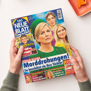 Diagonal fotografiertes Magazin „DAS NEUE BLATT – Das Original!“ in zwei Händen vor weißem Hintergrund. Das Cover zeigt drei weibliche und eine männliche Person sowie die Überschrift „Morddrohungen! So beschützt sie ihre Töchter“; weitere lesbare Texte: „KÖNIGIN MÁXIMA“, „Bewegende Botschaft ANNA ERMAKOVA“, „In der Psycho-Falle MICHELLE“, „Käsekuchen mit Lieblings-Früchten“ und „Sommer-Salate“.