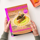 Das Magazin „FEINSCHMECKER“ liegt schräg auf einer weißen Fläche und wird von zwei Händen mit grauen Strickärmeln gehalten. Das orangefarbene Cover zeigt ein angerichtetes Fischgericht und trägt die Texte „Bodensee in Bestform“, „20 Top-Adressen: Moderne Fischküche, Hotels mit Charme und Einkaufstipps“, „Portugals Genuss-Oasen“, „Neue Küchenwelten“ sowie „Mit Special Seiser Alm: Lokale, Hütten, Feinkost“.