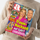 Weibliche Person im beigefarbenen Strickpullover hält ein schräg fotografiertes, glänzendes Magazin mit rotem, pinkem und blauem Cover. Sichtbare Texte: „die aktuelle“, „Rätsel-Magazin“, „Traum-Hochzeit auf Sylt?“, „Julia Klöckner & Jörg Pilawa“, „Florian Silbereisen“ und „Heidi Klum – Große Sorgen um Mama Erna“; abgebildet sind mehrere Frauen und Männer.