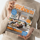Zwei Hände in beigefarbenem Strickpullover halten die Zeitschrift „Zuhause Wohnen – Wie Wohnen wirklich glücklich macht“, Ausgabe Juli 2026. Das Cover zeigt ein modern eingerichtetes Wohnzimmer mit grauem Sofa, Holztisch, beigen Kissen und großer Fensterfront. Sichtbare Schlagzeilen: „Kleine Räume, viel Platz“, „Lust auf Süden“, „Kühle Träume“, „Zaubern mit Tapeten“ und „Zu gewinnen“.