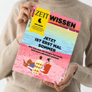 Person mit beigefarbenem Strickpullover hält das Magazin „ZEIT Wissen“ (Ausgabe Juli/August 2023) in den Händen; Titelseite mit gelbem Feld „DER MOND – Die große Kraft am Himmel und ihr Einfluss auf die Menschen“ sowie Hauptüberschrift „JETZT IST ERST MAL SOMMER. Wie man sich von Sorgen frei macht. Und neue Lebenslust gewinnt.“; Illustration eines Paares auf Liegestühlen am pinkfarbenen Strand mit blauem Meer und hellem Himmel im Hintergrund.