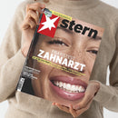 Person mit beigefarbenem Strickpullover hält eine Ausgabe des Magazins „stern“ in den Händen; Titelbild zeigt ein nahes Porträt einer lachenden Person mit Sommersprossen, großem weißen Schriftzug „Praxistest Zahnarzt“ sowie weiteren Texten: „Der große stern-Report: Zu hohe Rechnungen, falsche Behandlungen – und ein Ausweg“, „Katherina Reiche“, „Russlands Epstein-Skandal“ und oben grünem Hinweisfeld zur „Fußball-EM 2024“.