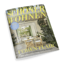 Titelbild der Wohnzeitschrift „SCHÖNER WOHNEN“ mit großem gelbem Schriftzug auf einem Foto einer überdachten Terrasse mit Holzstühlen, weißen Sitzpolstern und gedecktem Tisch vor grünem Gartenblick; Textaufschriften u. a.: „FERIEN-FLAIR – Sommerhäuser von Dänemark bis Marokko“, „Erfrisch aufwachen – Großer Schlafguide für heiße Nächte“, „Komfortzone – Neue Sofas und Sessel voller Polster-Power“, „An der Garden Route – Ein grünes Paradies in Südafrika“.