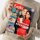 Person in beigefarbenem Strickpullover hält eine Ausgabe des Magazins „Gala“ mit rotem Titelkopf. Auf dem Cover umarmt eine hellhaarige Frau in schwarzem Kleid eine dunkelhaarige Frau in rotem Blazer, dazu die weiße Überschrift „Kraftvolle Rückkehr“. Weitere sichtbare Texte: „Applaus & Protest“, „Sie will es allen beweisen“, „Adele“, „Lucy Diakovska“ und „Wedding Issue“ auf rosafarbener Plakette oben rechts.