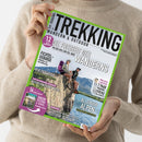 Person in beigem Strickpullover hält eine Outdoor-Zeitschrift mit grünem Rand und dem Titel „TREKKING – WANDERN & OUTDOOR“. Auf dem Cover sitzen zwei wandernde Personen mit Rucksäcken auf einem Felsen vor Bergkulisse. Textelemente: „DIE FREIHEIT DES WANDERNS“, „Fichtelgebirge“, „Via Paradiso“, „Norwegens raue Natur“, „Allgäuer Alpen“ und Hinweise auf 12 Tourentipps, Gewinnspiel und ein „Green Outdoor & Travel“-Spezial.