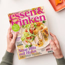 Kochzeitschrift „essen & trinken“ mit pinkem Titel, von zwei Händen vor hellem Hintergrund gehalten. Das Cover zeigt einen Teller mit Salat, Gemüse, Geflügel und Garnelen sowie Texte wie „Aus Liebe zum Kochen“, „Saucen-Schule“, „Neue Hits mit Huhn“ und „www.essen-und-trinken.de“; oben rechts liegt ein oranges Tablett mit Küchenutensil.