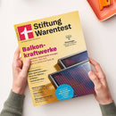 Titelblatt der Zeitschrift „Stiftung Warentest“ mit gelbem Hintergrund, großem weißen Logo auf rotem Feld links oben und Überschrift „Balkonkraftwerke“ in violetter Schrift. Weitere sichtbare Texte: „Geprüften Solarmodule erzeugen Strom“, „Klimaanlagen“, „Smartwatches“, „Akku-Bohrschrauber“, „Deos für Männer“, „Grillkäse“. Unten rechts sind zwei geneigte Solarmodule mit dunklen, reflektierenden Oberflächen abgebildet, gehalten von zwei Händen.