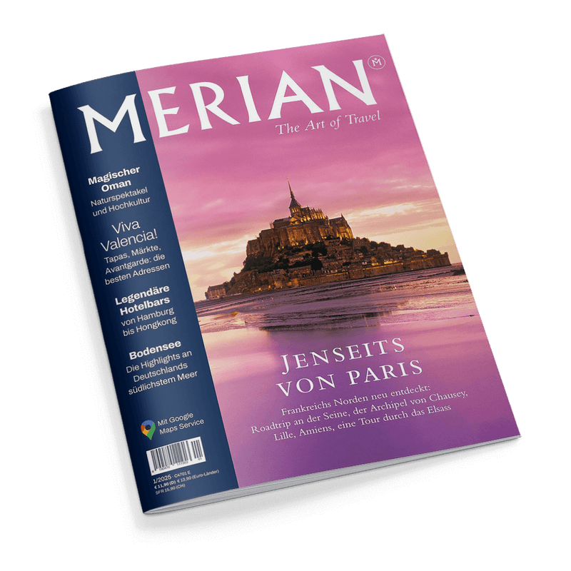 Reisemagazin „MERIAN – The Art of Travel“ mit violettem Cover, zentralem Foto der Abtei Mont-Saint-Michel bei Sonnenuntergang, darüber der Titel „JENSEITS VON PARIS“ und Unterzeile zu Reisezielen in Nordfrankreich; linke Spalte mit Themenvorschau u. a. „Magischer Oman“, „Viva Valencia!“, „Legendäre Hotelbars“ und „Bodensee“, Logo „Mit Google Maps Service“ unten links.