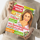 Person mit beigefarbenem Strickpullover hält die Zeitschrift „Fernsehwoche“ mit rotem Herzlogo und weißrotem Titel. Auf dem Cover eine lächelnde Frau mit hellbraunen Haaren vor hellem Hintergrund. Schlagzeilen u. a.: „Mit Naturmedizin zu innerer Ruhe“, „Cremiger Apfel-Käsekuchen“, „Die besten Tipps für ein kräftiges Herz“, „Geld zurück dank Sammelklage“ und „Traumhaft schöne Ideen mit Margeriten“.