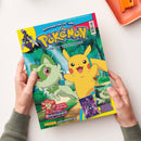 Hände einer Person mit grünem Strickpullover halten ein farbiges Magazin mit der Aufschrift „Pokémon – Das offizielle Magazin“. Auf dem Titel sind die Figuren Pikachu in Gelb und Felori in Grün vor einem Waldhintergrund abgebildet. Weitere sichtbare Texte: „Schnapp sie dir alle!“, „Die besten Spielzeuge aus Paradoxrift“, „Coole Poster“, unten das Panini-Logo und die Website „www.pokemon.de“.