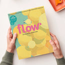 Bunt gestaltetes Magazin „flow“ mit gelber, türkisfarbener und grüner Blättermuster-Collage, großer pinker Titelaufschrift und dem Untertitel „Do what you love and turn today.“ Oben steht „Das Magazin für persönliche Entwicklung, Kreativität & mehr Ruhe“; zwei Hände halten das Magazin vor hellem Hintergrund, daneben liegt oben rechts ein orangefarbenes Schreibutensil.