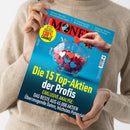Weibliche Person im hellbeigen Strickpullover hält eine schräg ausgerichtete Zeitschrift mit türkisfarbenem Cover. Darauf stehen „MONEY“, „Die 15 Top-Aktien der Profis“, „EXKLUSIVE ANALYSE“ und „DAS BESTE AUS 45.000 AKTIEN“; abgebildet sind ein transparentes Sparschwein mit roten, rosa, weißen und blauen Herzen sowie eine Hand mit rotem Herz.