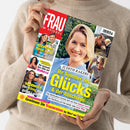 Eine weibliche Person im beigefarbenen Strickpullover hält ein schräg abgebildetes Magazin „FRAU IM SPIEGEL“ mit rotem Titelkopf. Das Cover zeigt Judith Rakers sowie die Texte „Ihr Sommer des Glücks & der Abschiede“, „Thomas Müller – Neue Liebe für den Fußball-Star?“, „Christine Neubauer – Sie verkauft ihre Villa auf Mallorca“ und „Kate & Louis – Der König der guten Laune“.
