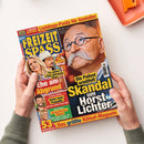 Zwei Hände mit grauen Strickärmeln halten schräg eine farbige Zeitschrift vor weißem Hintergrund; oben rechts liegt ein orangefarbenes Tablett. Auf dem Cover stehen „FREIZEIT SPASS“, „7 SEITEN EXTRA“, „Lieblings-Pasta für Genießer“, „Die besten Rätsel“, „Ehe am Abgrund“ und „Die Polizei ermittelt: Skandal um Horst Lichter“; abgebildet sind mehrere Personen, darunter ein Mann mit Brille und Schnurrbart.