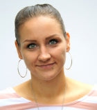 Frau mit zurückgebundenen Haaren und Ohrringen mit einem rosa weiß gestreiften Shirt.