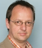 Mann mit Brille und kurzem Haar blickt in die Kamera.