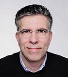 Porträt eines freundlich blickenden Mannes mit Brille.