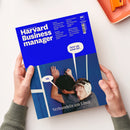 Blaues Magazin „Harvard Business manager“ mit dem Untertitel „Das Wissen der Besten“, von zwei Händen vor hellem Hintergrund gehalten; oben rechts HBR-Logo. Sichtbare Texte: „Wie Game Boy und Crocs zu Ikonen wurden“, „Warum Ikea Chatbots umgarnt“, „Zahlen sich immersive Erlebnisse aus?“, „Wann es Zeit ist, Prioritäten neu zu setzen“, „Jetzt gib schon auf…“, „Nö.“ und „Verhandeln am Limit“; darunter zwei männliche Personen, eine mit weißem Kopfschutz.