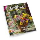 Schräg fotografierte Ausgabe der Zeitschrift „Landlust“ mit schwarzem Cover und großem weißem Titel. Darauf ein herbstlicher Blumenstrauß in einem braunen Gefäß, links drei kleine Bildfelder mit Getränk, Hirsch und Gebäck sowie die Texte „NEUE STRICKIDEEN“, „Laubsammler: Aufsatz für Schubkarren bauen“, „Basteln: Blüten aus Kieferzapfen“, „Unverzichtbare Ehrenamtliche Bürgermeister“ und „Der Herbst zieht ein“.