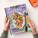 Auf weißer Fläche hält eine Person mit grauen Strickärmeln das schräg liegende Magazin „Lust auf Genuss“ mit lila Cover. Sichtbar sind ein Teller mit gebratenem Geflügel und Gemüse, Brot, Kräuter sowie die Texte „BONJOUR PROVENCE“, „Von Ratatouille über Quiche bis Tarte au citron“ und „DAS BESTE AUS SÜDFRANKREICH“; oben rechts liegt ein orangefarbenes Tablett.