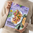 Eine Person im beigefarbenen Strickpullover hält ein schräg abgebildetes Kochmagazin mit violettem Cover. Sichtbare Texte: „Lust auf Genuss“, „Das Beste aus Südfrankreich“, „Bonjour Provence“, „Von Ratatouille über Quiche bis Tarte au citron“ und „Coq au vin rosé mit Estragon-Pistou“; abgebildet sind ein Teller mit gebratenem Geflügel und Gemüse, Lavendel, Artischocken und eine Tarte.