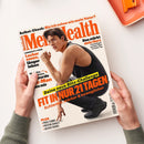 „Men’s Health“-Magazin, schräg von oben fotografiert und von zwei Händen mit grauen Ärmeln gehalten. Das Cover zeigt eine männliche Person in schwarzer Sportkleidung sowie die Texte „Selbst-Check: Bin ich schon wie mein Vater?“, „Das stärkt dein Herz“, „Longevity-Food: Lecker essen, länger leben“, „FIT IN NUR 21 TAGEN“ und „PLUS Padel-Tennis, Protein-Shakes, Jacken-Trends“; oben rechts liegt ein orangefarbenes Objekt.