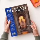 Schräg gehaltenes Magazin „MERIAN“ mit weißem Titel und dem Zusatz „The Art of Travel“. Das Cover zeigt einen steinernen Torbogen mit Blick auf ein Gebäude bei Sonnenuntergang; links stehen „Albanien“, „Finnland“, „Bunte Städte“, „Lüneburger Heide“ und „Istrien“, darunter „OH EUROPA!“. Zwei Hände einer nicht eindeutig erkennbaren Person halten das Magazin; oben rechts liegt ein orangefarbenes Notizbuch.