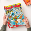 Schräg gehaltenes „MICKEY MAUS“-Magazin mit gelbem Titelbereich, rotem Logo und Comicillustration von Donald Duck und weiteren Enten in einem aufgebrochenen Tresor mit herumfliegenden Münzen. Sichtbare Texte: „TOP-COMIC: GENIALE GELDWÄSCHE“, „W.I.T.“, „SPIEGEL-TRICK“, „MAGAZIN“ und „EGMONT“; zwei Hände halten das Heft über einer weißen Fläche, oben rechts liegt ein orangefarbenes Tablett.