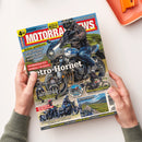 Schräg fotografierte Motorradzeitschrift „MOTORRAD NEWS“ in zwei Händen vor weißem Hintergrund. Das Cover zeigt eine motorradfahrende Person auf einem Honda-Motorrad sowie weitere Motorräder und Landschaftsaufnahmen; sichtbare Texte: „Service: Motorrad und Hitze“, „Schon gefahren!“, „KTM 790 Duke“, „Norton Atlas“, „SOUS S 2000 GL“, „Retro-Hornet“, „Fahrbericht: Honda CB 1000 F“, „Reisetipp: Schottland & Türkei“ und „Schöner Schottern“.