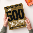 Braun-goldene Ausgabe des Musikmagazins „musikexpress“, von zwei Händen über einer weißen Fläche gehalten; oben rechts liegt teilweise ein orangefarbener Gegenstand. Sichtbare Texte: „musikexpress.de“, „musikexpress“, „DIE“, „Viel Stoff für deine Playlist!“, „500“, „BESTEN ALBEN ALLER ZEITEN“, „TEIL 1 DAS GROSSE RANKING“ und „ALLE PLATTEN NEU GEHÖRT, NEU BEWERTET“.